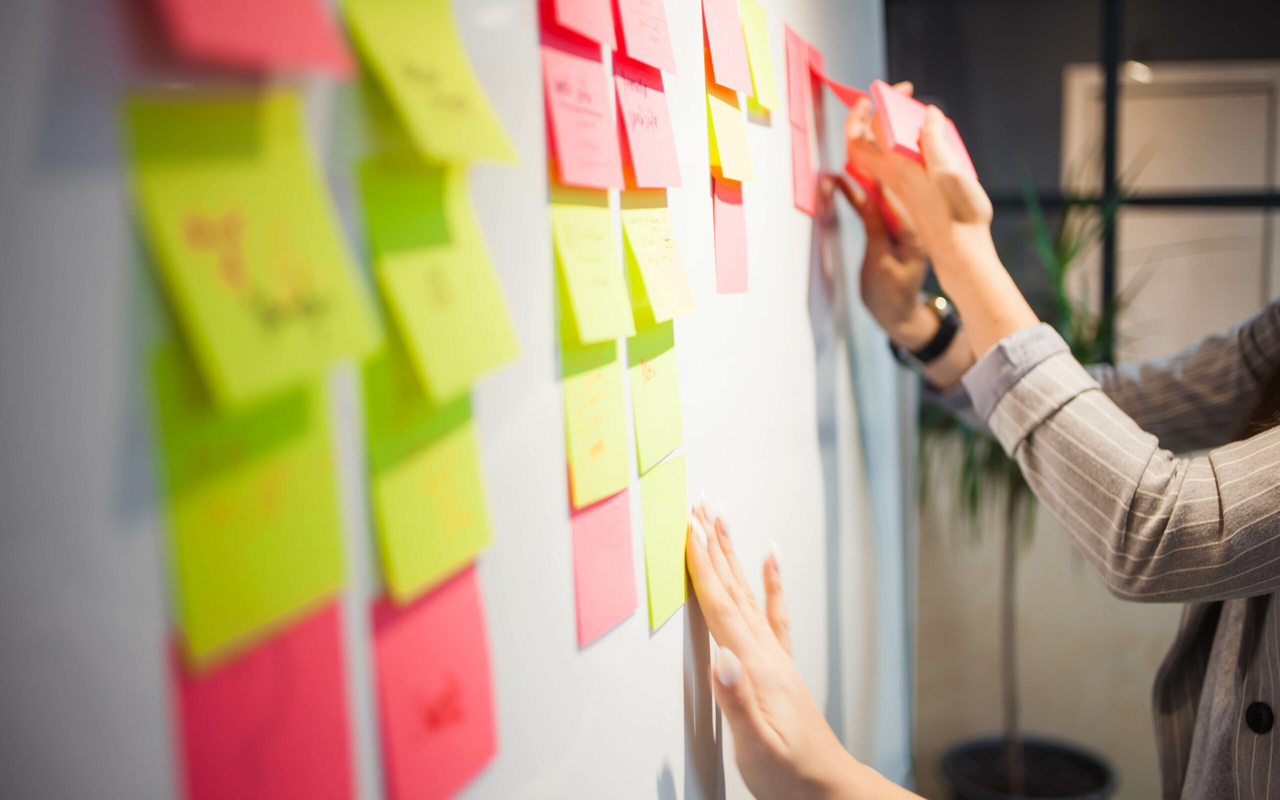 Eine Person klebt bunte Haftnotizen an eine Wand, um Ideen zu sammeln oder zu organisieren.